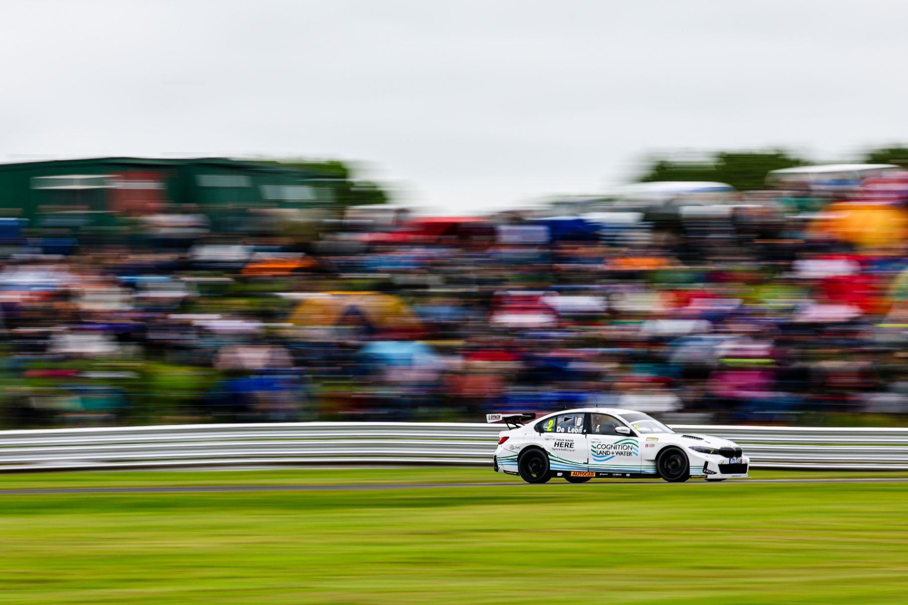 BTCC car racing past packed grandstands